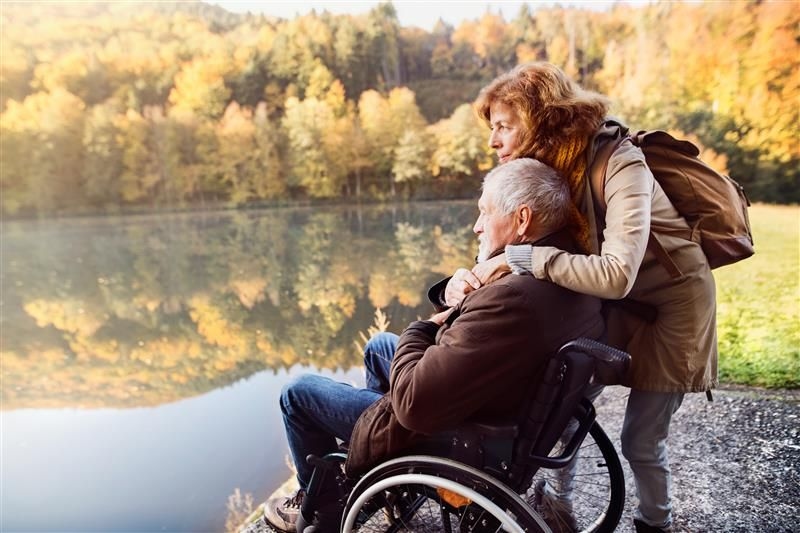 woman hugging man in wheelchair by a lake
